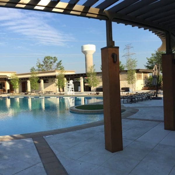 Outdoor swimming pool area under steel and wood structural canopy, and a modern building featuring striking CES architectural design in the background on a sunny day