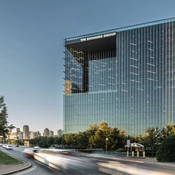 Exterior view of the building with the Dallas skyline in the background, showcasing the seamless glass curtainwall and sunshades designed in collaboration with Childress Engineering